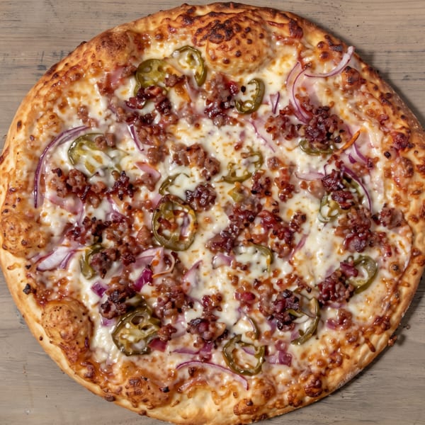 Round pizza with melted cheese, crumbled meat, red onions, and green jalapeños on wood.